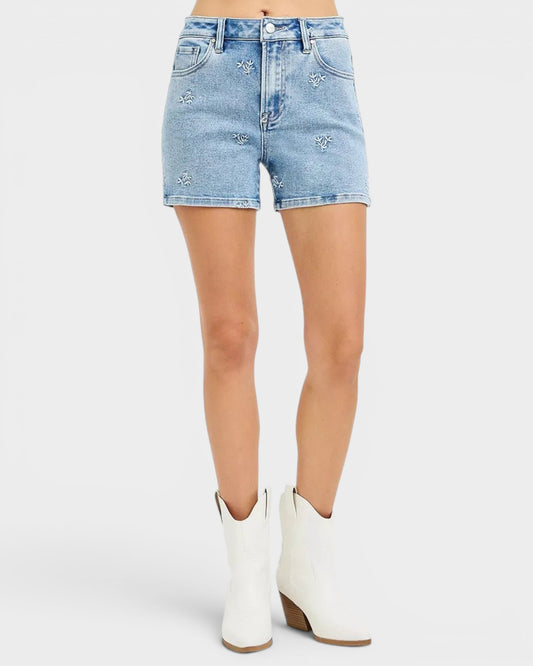 Beach Rose Co. light wash denim shorts with white embroidered floral details, high-rise fit, and short length.
