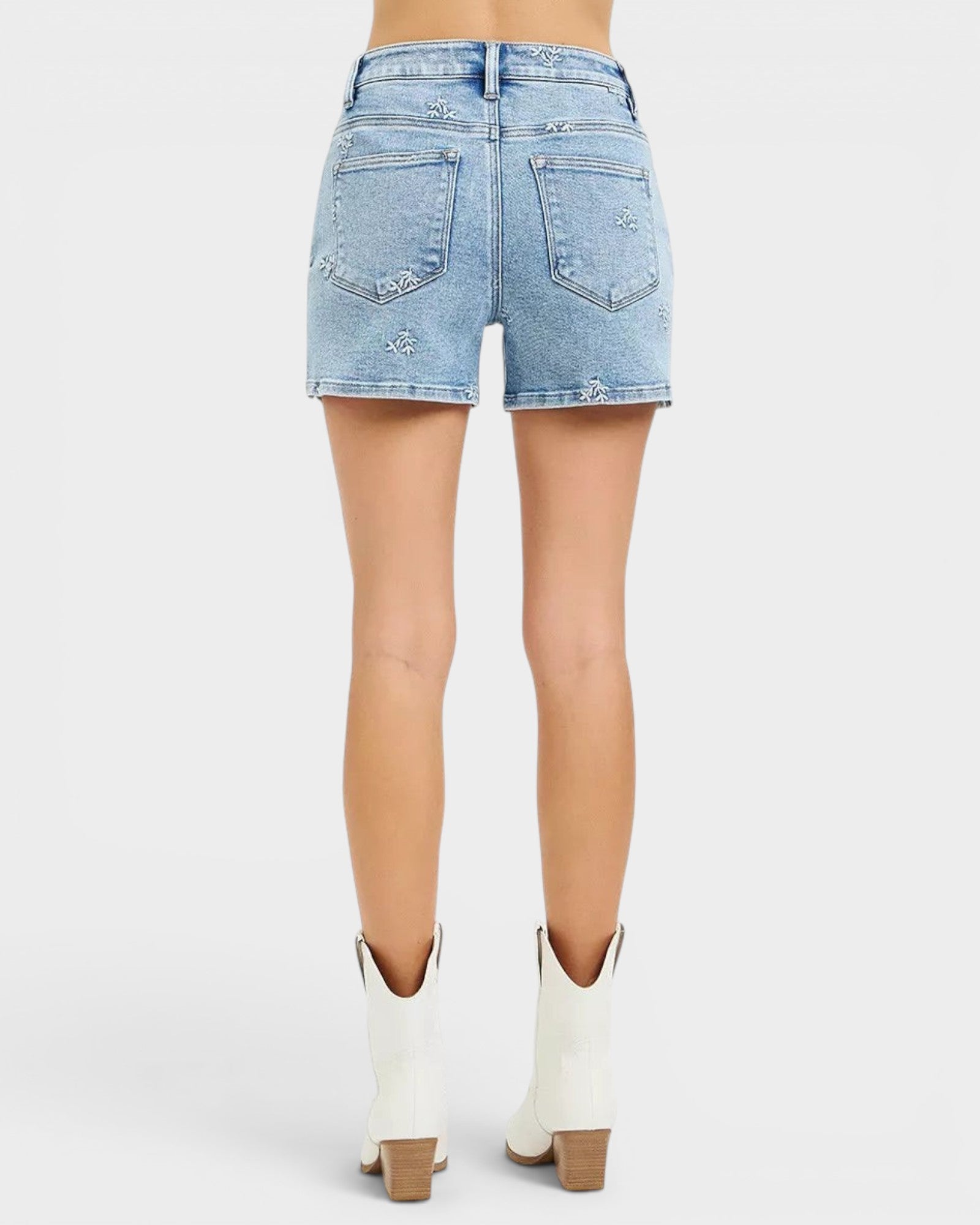 Beach Rose Co. light wash denim shorts with white embroidered floral details, high-rise fit, and short length.