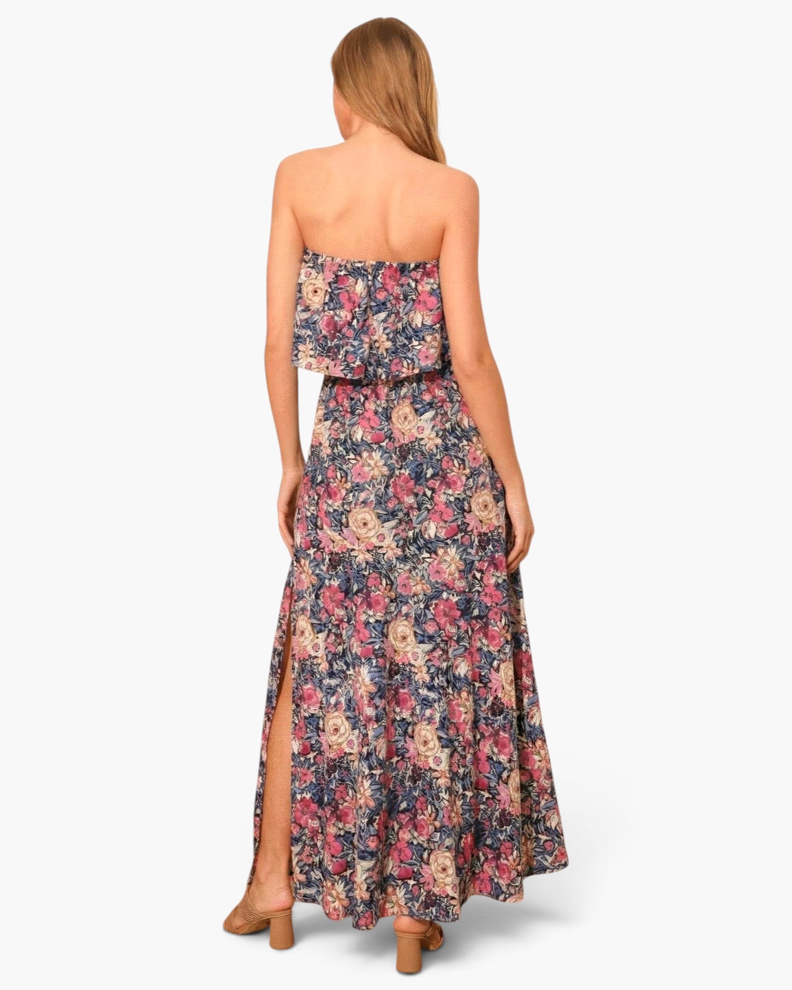Back view of a Beach Rose Co. strapless maxi dress featuring a vibrant floral print and a side slit on a model.