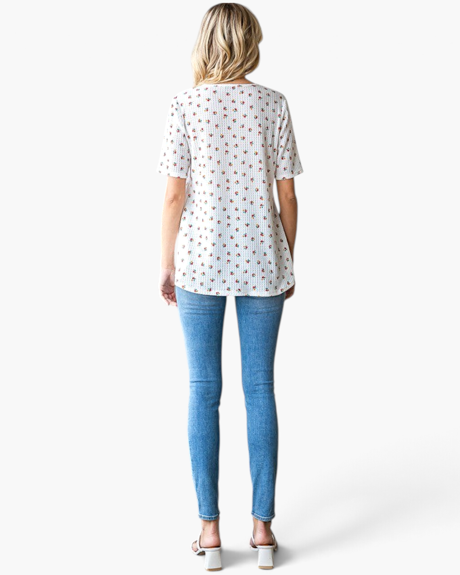 Back view of a woman wearing a Beach Rose Co. white ditsy floral textured knit tunic with short sleeves and blue jeans.