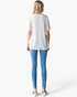 Back view of a woman wearing a Beach Rose Co. white ditsy floral textured knit tunic with short sleeves and blue jeans.