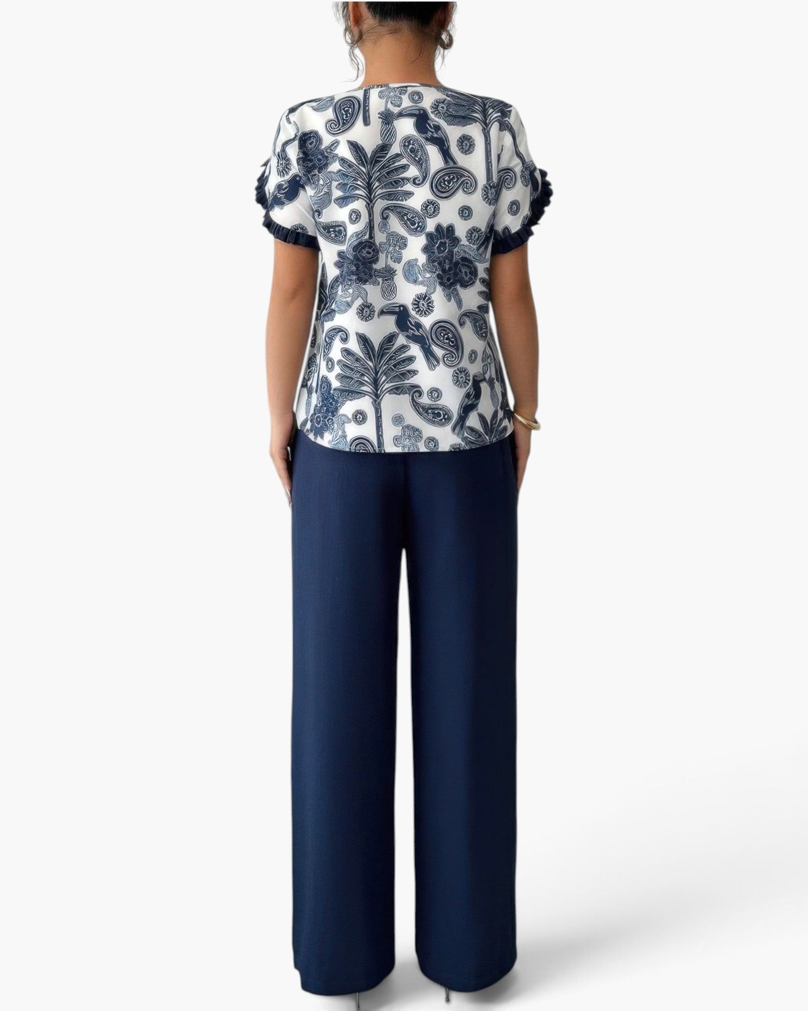 A woman shown from the back wearing a white short-sleeve top with a navy blue floral and paisley print, paired with navy blue wide-leg trousers, against a light gray studio background.