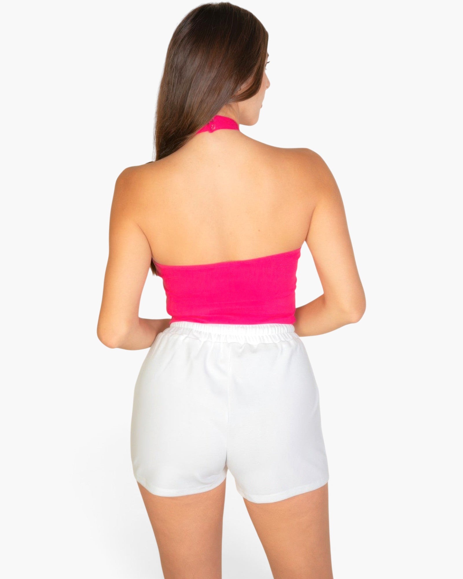 Beach Rose Co. model wearing a vibrant fuchsia ribbed halter neck backless crop top with white shorts