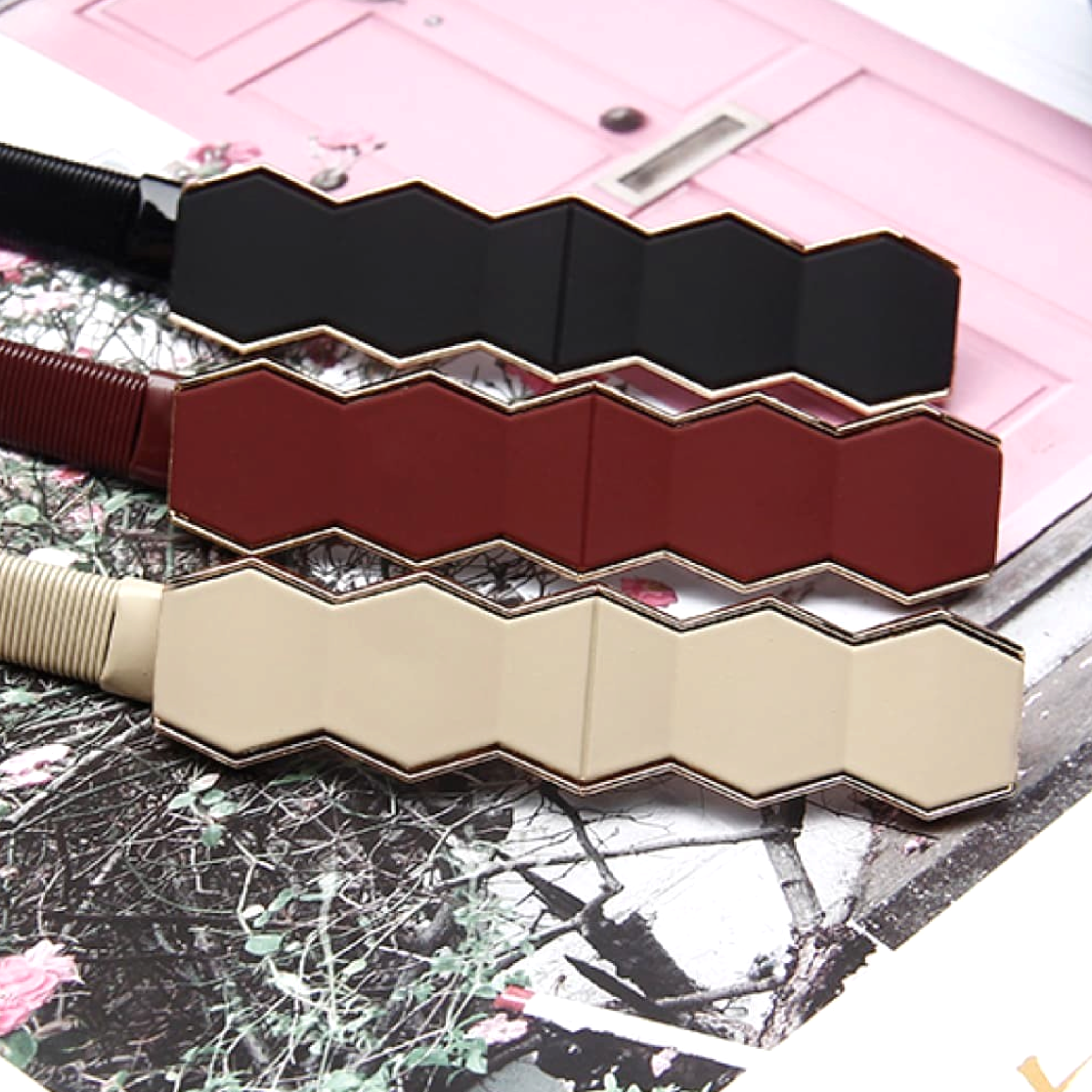 Beach Rose Co. skinny metal waist belts with geometric hexagon buckles in black, burgundy, and beige on a floral base.