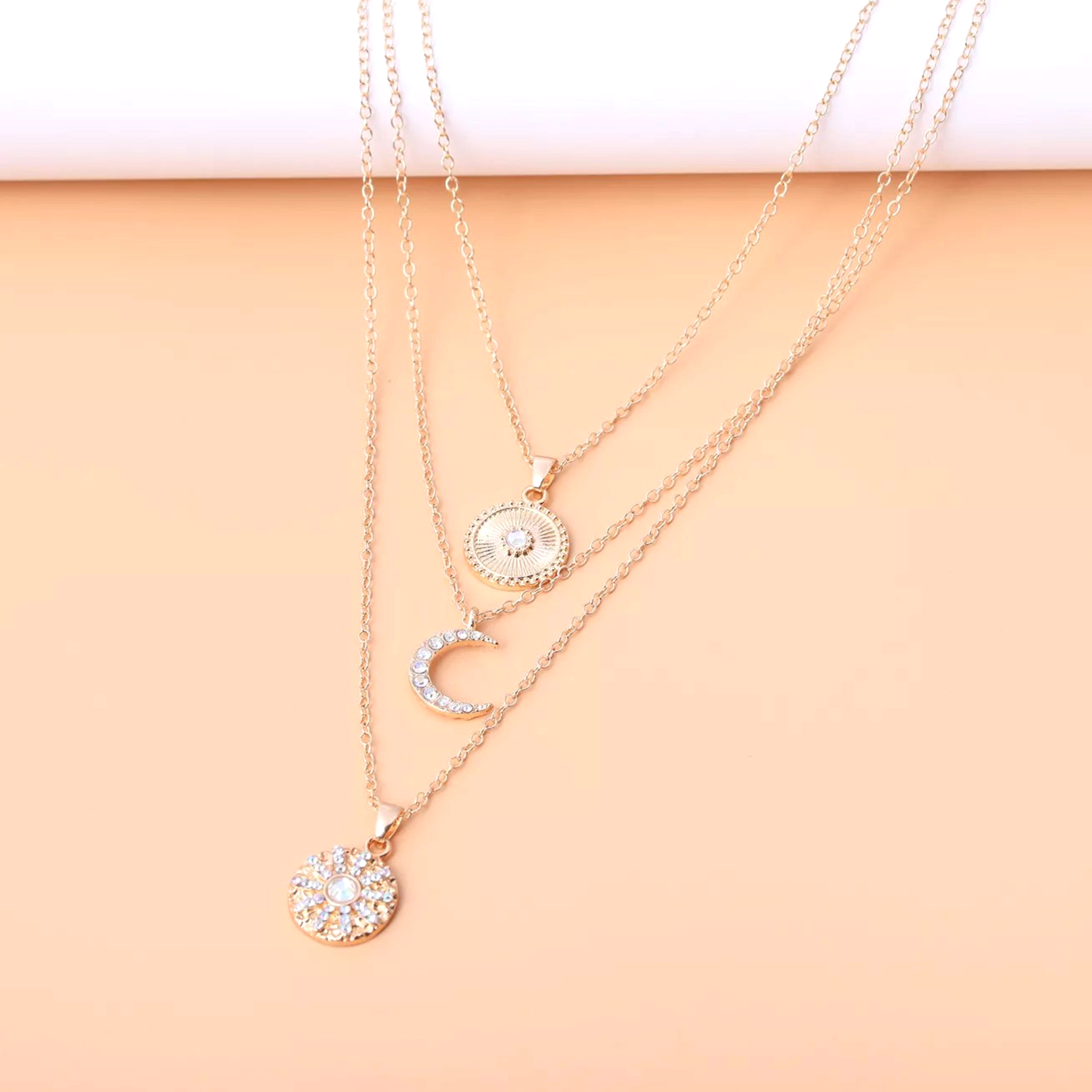 Beach Rose Co. 18K gold-plated layered necklace featuring sunburst, crescent moon, and zircon-accented pendants.