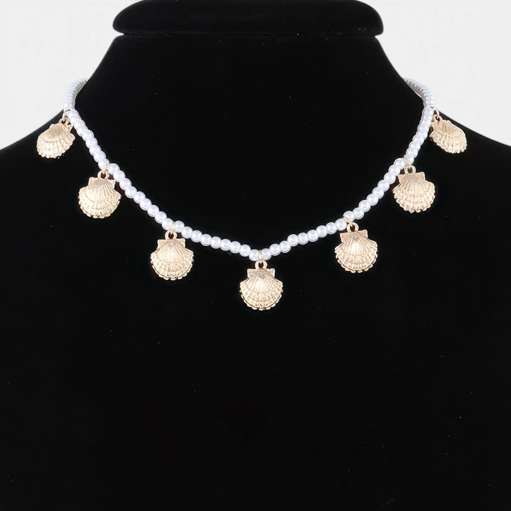 Beach Rose Co. gold clamshell charm necklace with white pearls on a black display bust