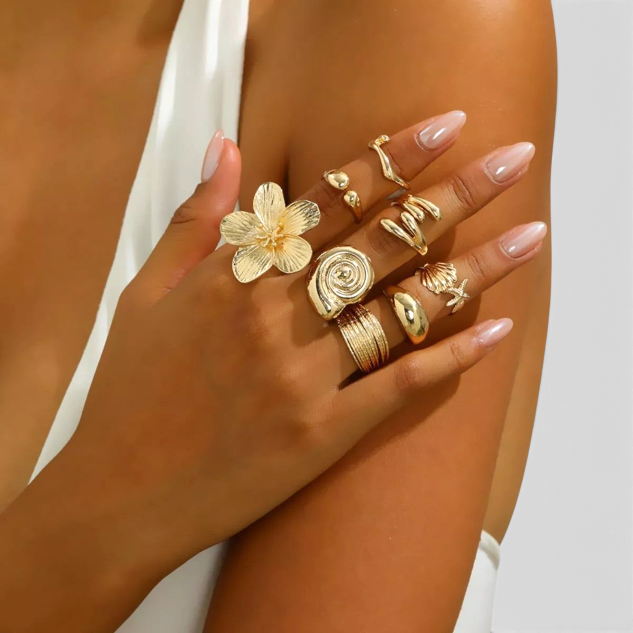 Beach Rose Co. 18K gold-plated ring set featuring sculptural flower, shell, and starfish designs on a model's hand.