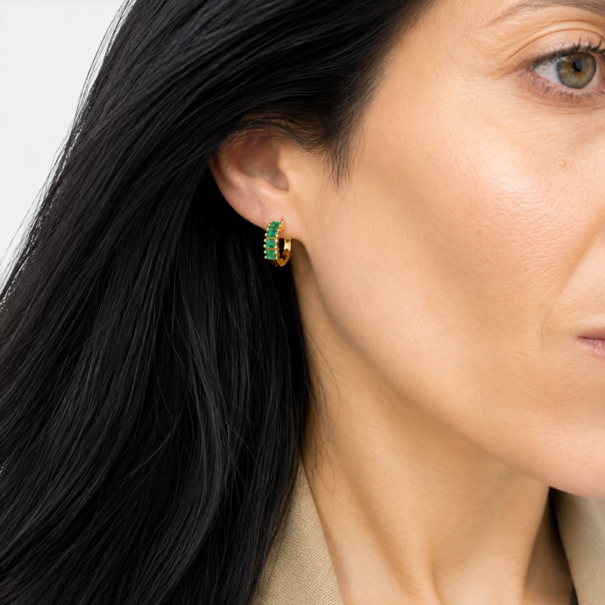 Beach Rose Co. gold huggie earrings featuring a row of emerald green baguette-cut cubic zirconia stones on a model.