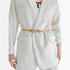 Beach Rose Co. slim gold metal waist belt with an intricate interwoven knot buckle worn over a white blazer.