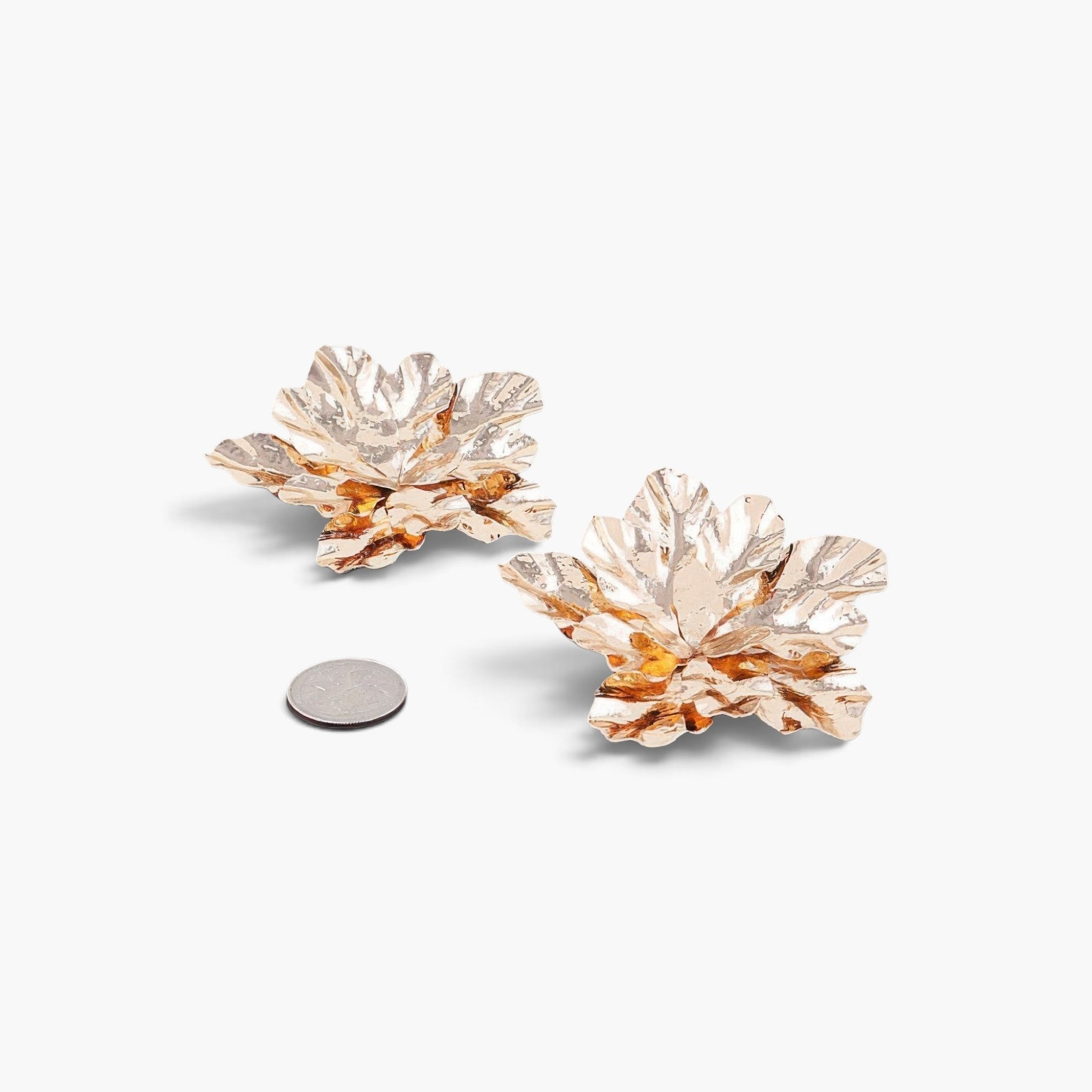Beach Rose Co. gold maple leaf earrings with intricate textured metal details, shown next to a coin for scale.
