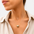 Beach Rose Co. gold puff heart pendant necklace worn on a delicate chain by a woman in a beige linen shirt.