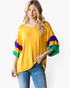 Beach Rose Co. gold top with purple and green color-block layered ruffle sleeves worn by a blonde model with jeans.