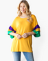 Beach Rose Co. gold top with purple and green layered ruffle sleeves and a relaxed fit worn by a smiling woman.