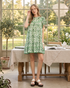 Beach Rose Co. green and cream floral mini dress with flutter sleeves and ruffled neckline in a sunlit garden room.