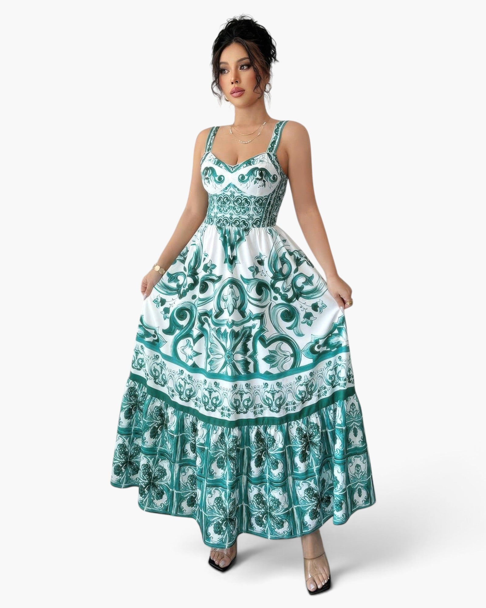 A woman modeling a sleeveless maxi dress with a white base and teal green baroque-style scroll pattern, set against a plain light gray studio background.