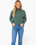 Beach Rose Co. green micro-stripe turtleneck top with dropped shoulders worn by a smiling blonde woman with blue jeans