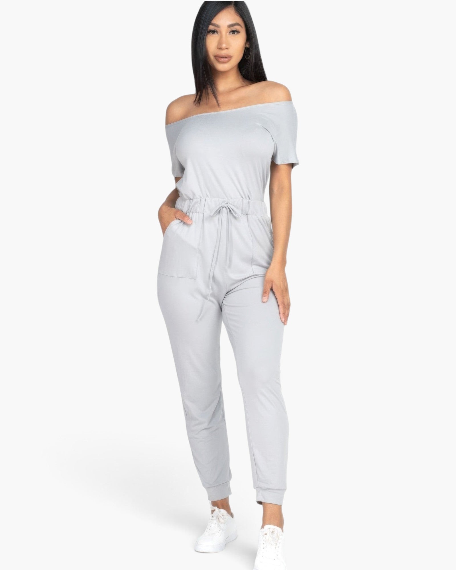 Beach Rose Co. grey off-the-shoulder drawstring jumpsuit in soft stretch jersey worn by a model with white sneakers.