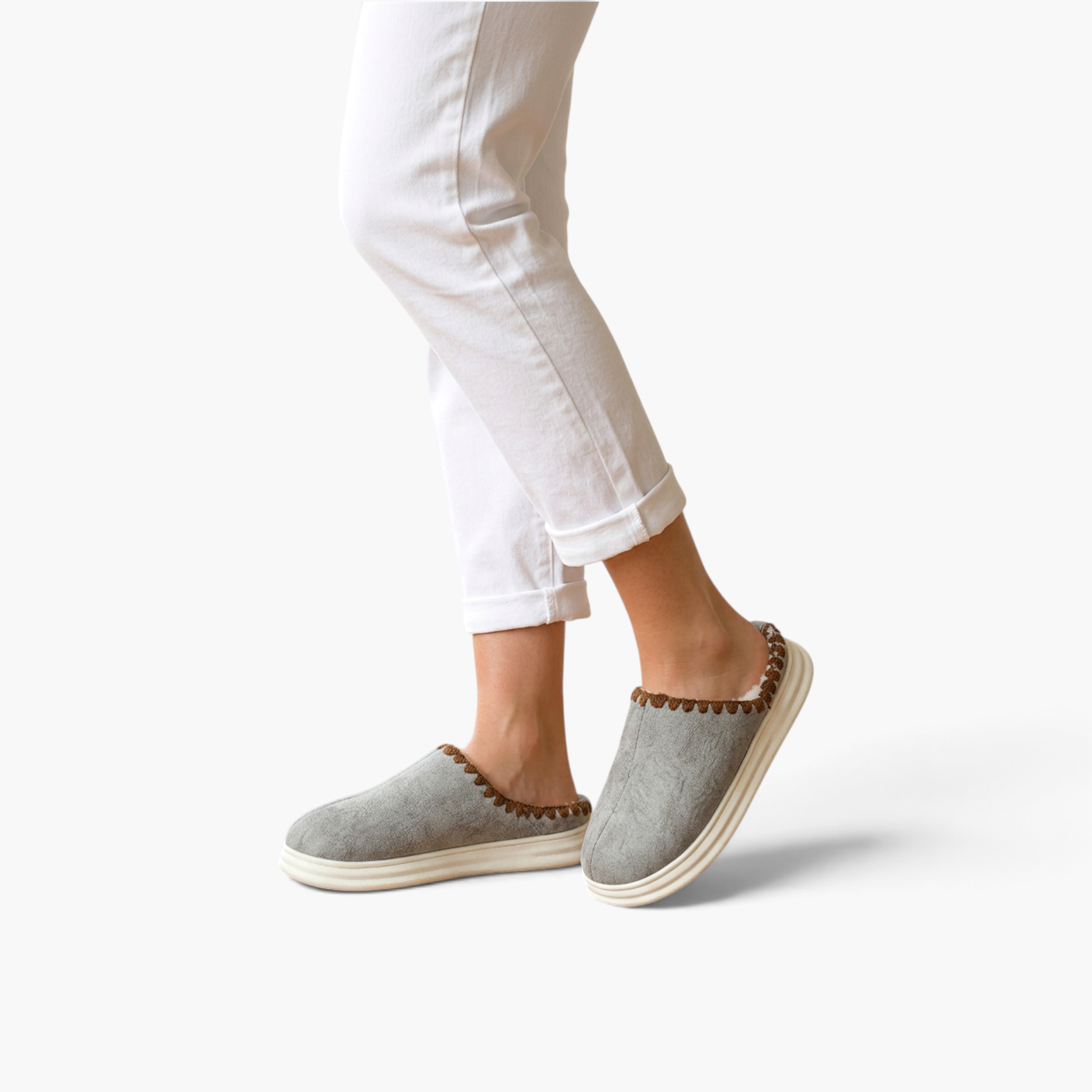 Beach Rose Co. Paula plush-lined grey slippers with thick soles and brown stitched trim worn with white trousers.
