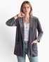 Beach Rose Co. grey velour open-front cardigan with patch pockets worn by a woman over a white tank top and jeans.