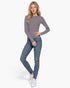 Beach Rose Co. model wearing a grey and white striped long sleeve crew neck sweater with blue jeans and white sneakers.
