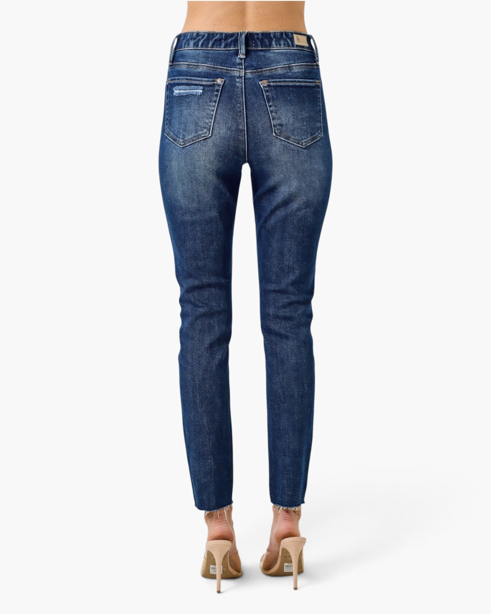 Beach Rose Co. dark wash high rise skinny jeans with frayed ankle hems and back pockets, worn with nude heels.