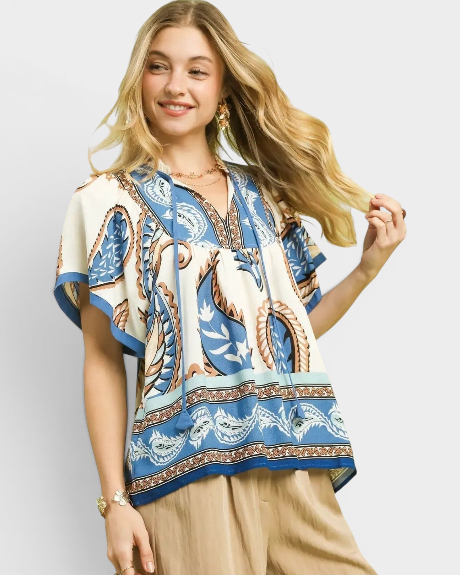 Beach Rose Co. ivory and blue paisley border print rayon top with tassel details and flutter sleeves.