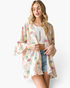 Beach Rose Co. ivory floral kimono with bell sleeves and an open-front design worn over a white tank top and shorts.