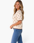 Beach Rose Co. ivory cotton knit top with brown polka dots, puff sleeves, and scalloped trim worn by a smiling model.