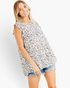 Beach Rose Co. ivory tiered top with black spotted print, flutter sleeves, and round neck worn with denim shorts.