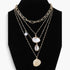 Beach Rose Co. layered gold chain necklace featuring seashell, starfish, and pearl charms on a black display bust.
