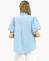 Back view of a Beach Rose Co. light blue textured blouse with a ruffled collar and puff sleeves on a model.