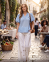 Beach Rose Co. light blue textured puff sleeve blouse with ruffle neck, worn with white eyelet pants in a cafe setting