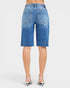 Beach Rose Co. Medium wash denim Bermuda shorts with raw hem and five-pocket styling. Made from a cotton blend with stretch.