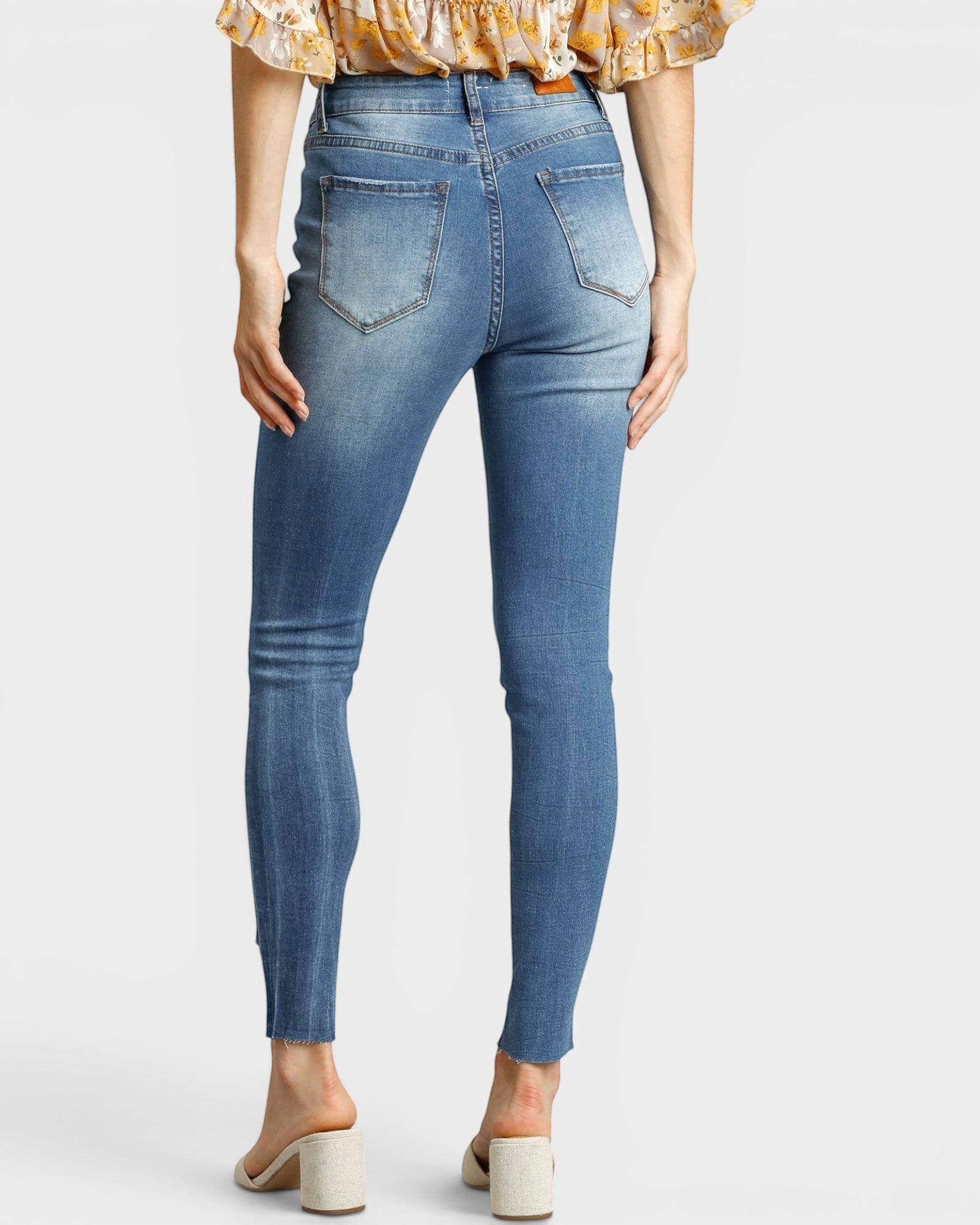 Beach Rose Co. medium wash skinny jeans with distressed details and raw ankle hem, made from cotton and spandex blend.