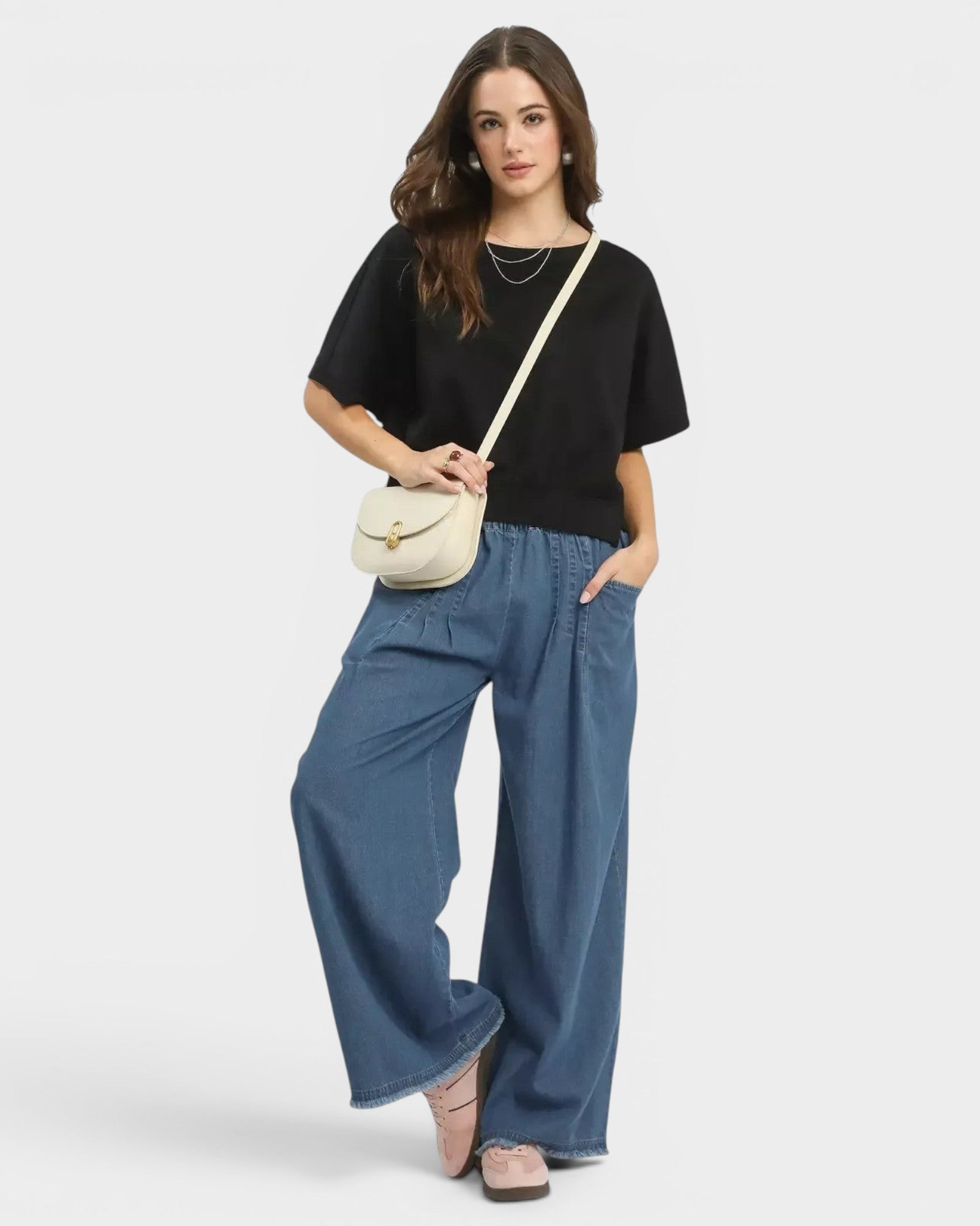 Beach Rose Co. medium wash 100% cotton wide leg jeans with raw hem and pockets. Model is wearing them with a black top and cream crossbody bag.