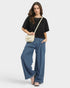 Beach Rose Co. medium wash 100% cotton wide leg jeans with raw hem and pockets. Model is wearing them with a black top and cream crossbody bag.