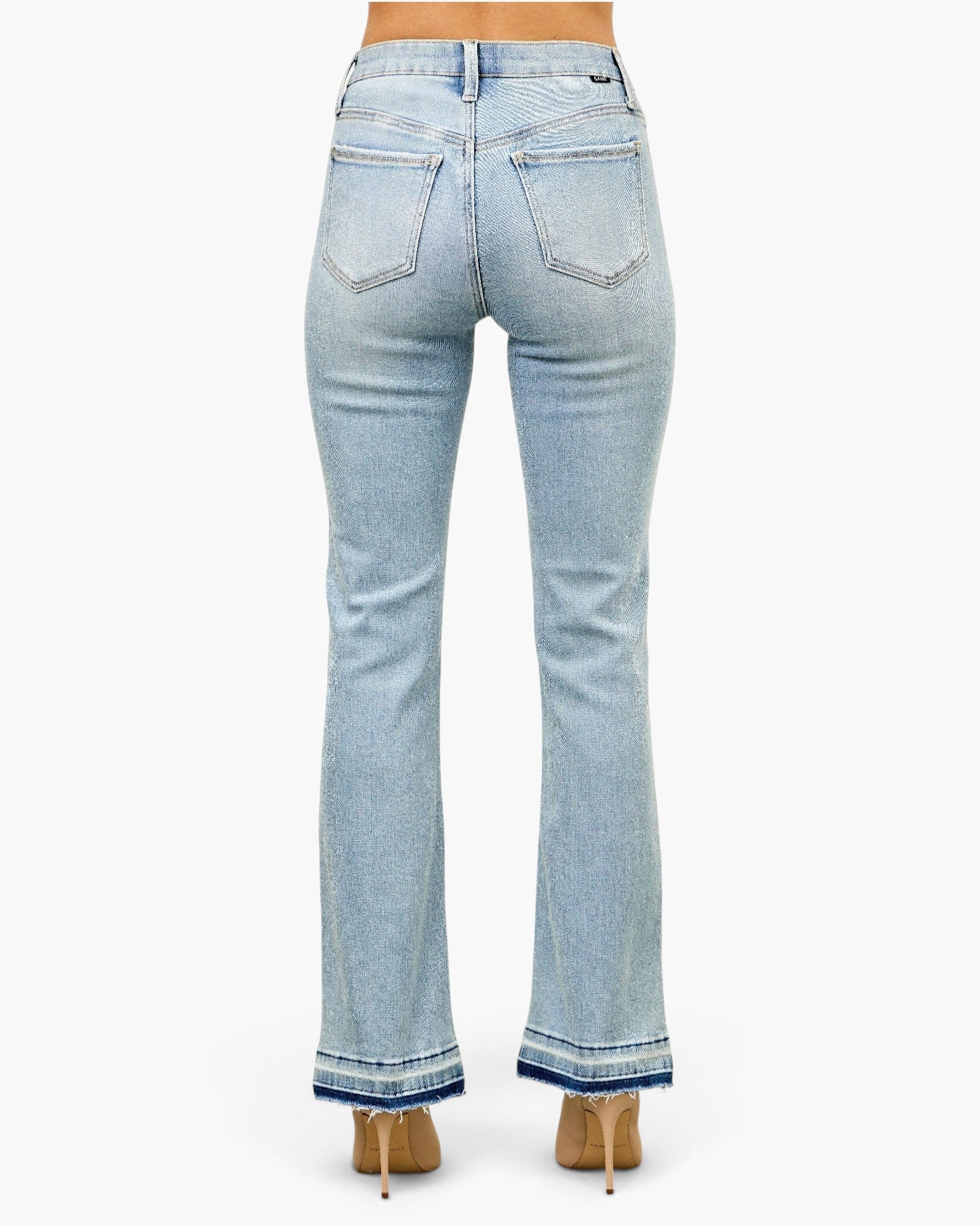 Beach Rose Co. light wash mid-rise flare jeans with a raw released hem, viewed from the back on a model in heels.