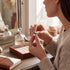 Beach Rose Co. 1 carat round moissanite stud earrings with four-prong settings held by a woman at a vanity table.