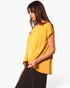 Beach Rose Co. mustard yellow washed poly silk tunic top with a tulip hemline worn by a model in a side view