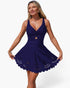 A woman modeling a short navy blue dress with a deep V-neckline, twisted front detail, a flared skirt, and scalloped eyelet trim, photographed against a plain light background.