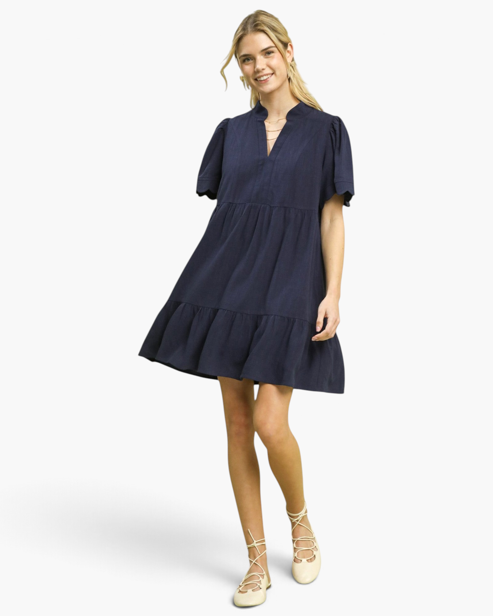 Model wearing a Beach Rose Co. navy linen blend mini dress with a tiered skirt, split neckline, and scalloped sleeves.