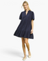 Model wearing a Beach Rose Co. navy linen blend mini dress with a tiered skirt, split neckline, and scalloped sleeves.