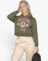 Beach Rose Co. olive green drop shoulder pullover hoodie with Chicago graphic, worn by a woman with headphones.