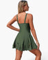 A woman modeling an olive green sleeveless mini dress from the back, featuring shoulder straps, a fitted bodice, and a flared skirt with decorative cutout details near the hem, set against a plain white background.