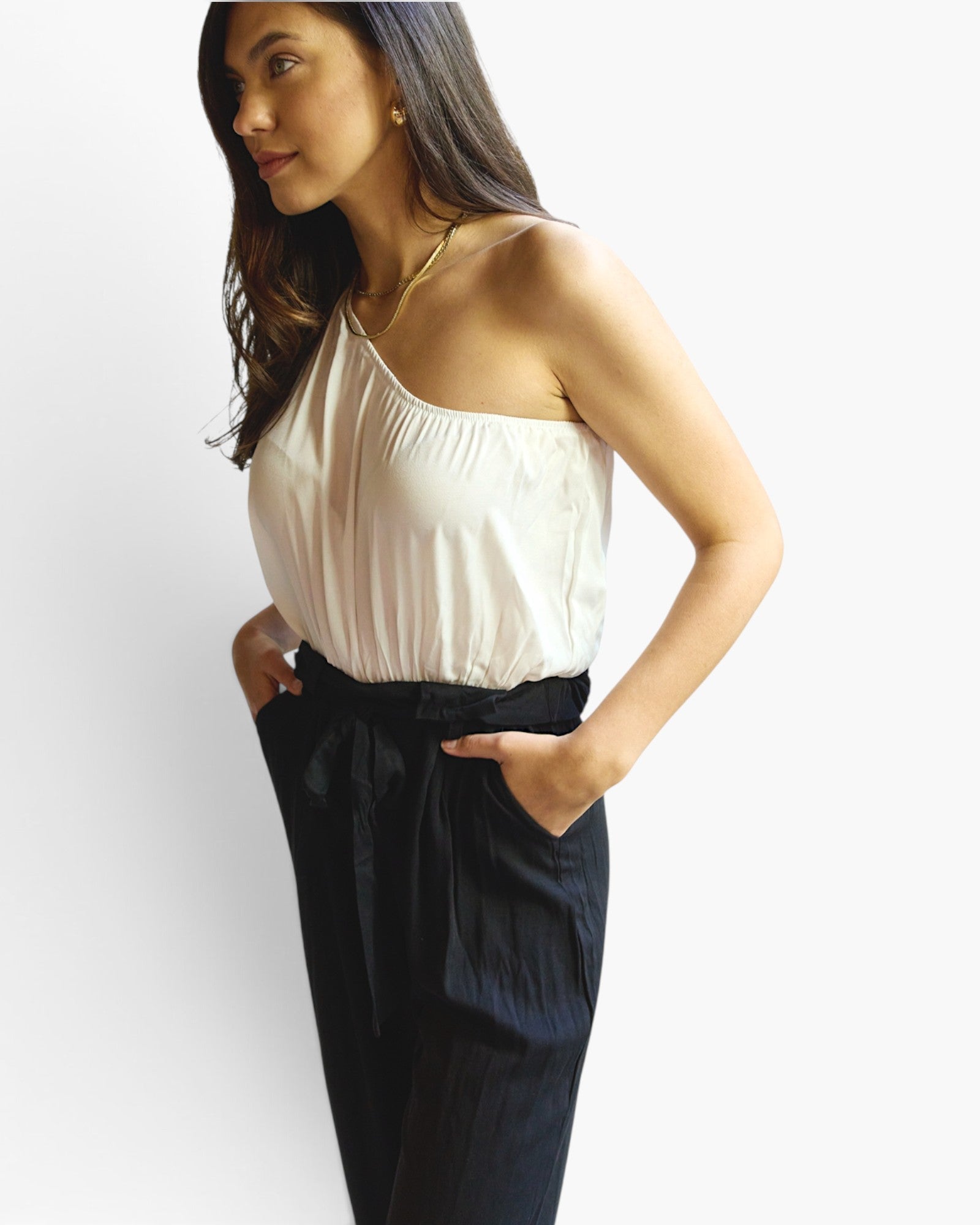 Beach Rose Co. white and black one-shoulder jumpsuit with a paperbag waist and side pockets on a model