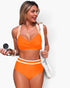 Beach Rose Co. orange high-waisted bikini with white trim and cross-front top worn by a woman holding a camera