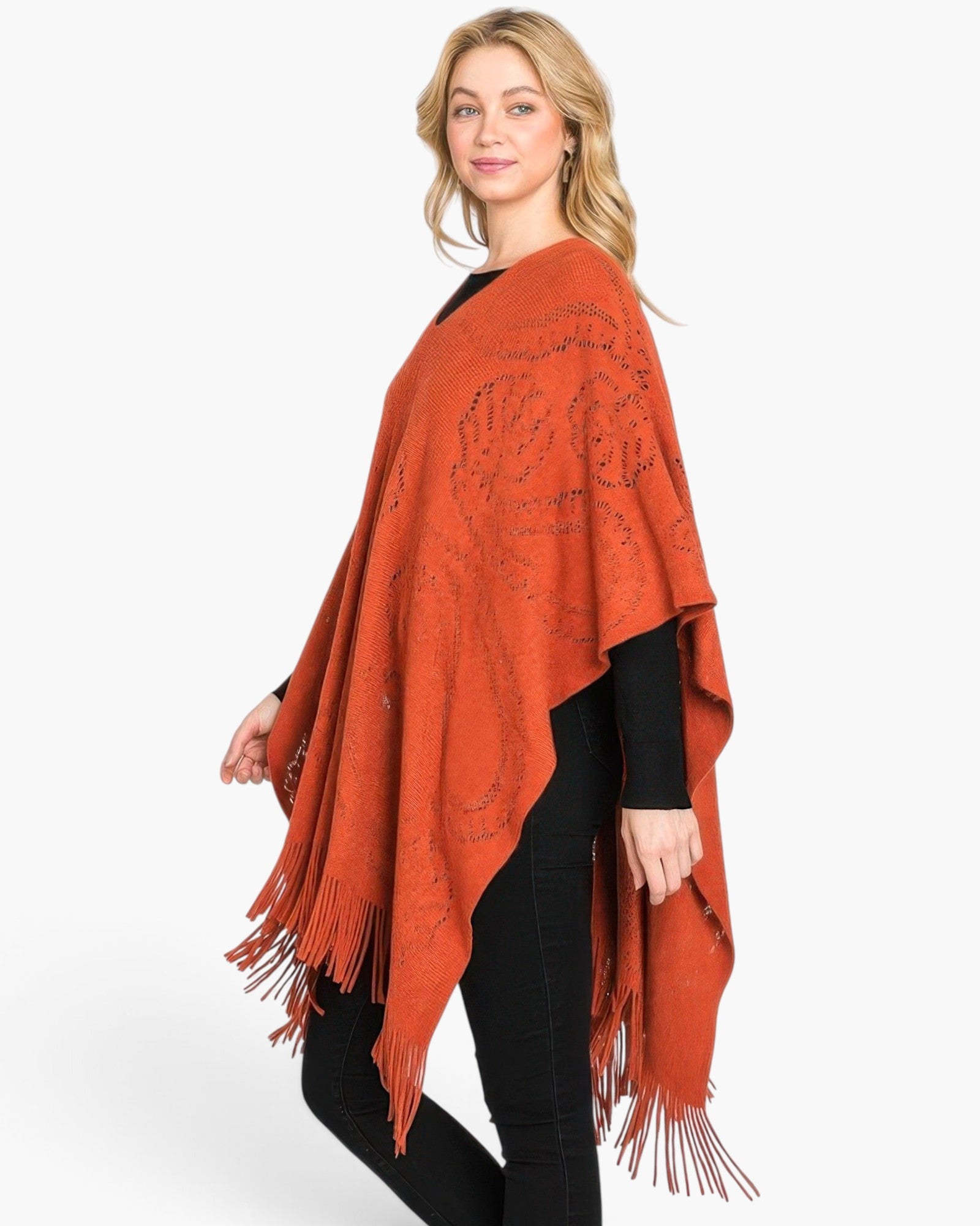 Beach Rose Co. model wearing a burnt orange acrylic paisley pattern poncho with fringe hem over a black outfit.