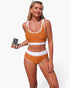 Beach Rose Co. orange polka-dot high-waisted bikini set with white contrast trim worn by a model holding a camera