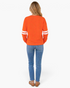Back view of a woman wearing a Beach Rose Co. orange sweatshirt with white varsity stripes on the sleeves.