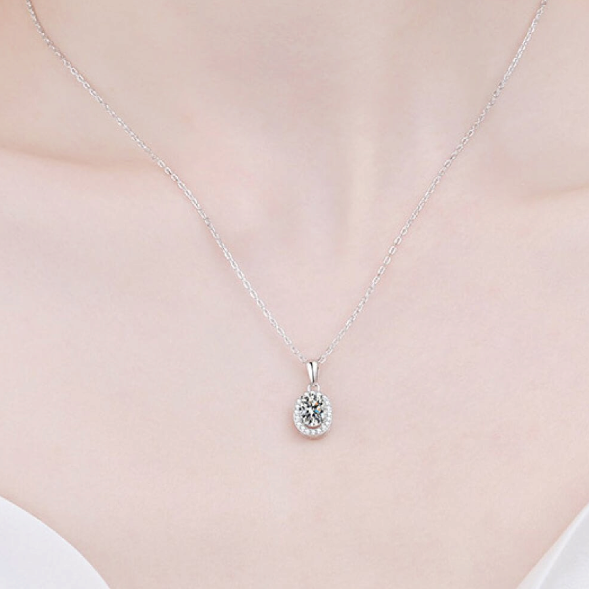 Beach Rose Co. silver oval moissanite halo pendant necklace on a delicate sterling silver chain worn on a neck.